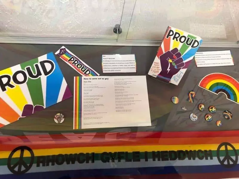Colourful collection of paraphernalia surrounding an anthology PROUD by Juno Dawson and featuring poem, How to come out as gay by Dean Atta